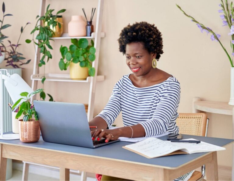 A woman works at a desk in a room decorated with plants.