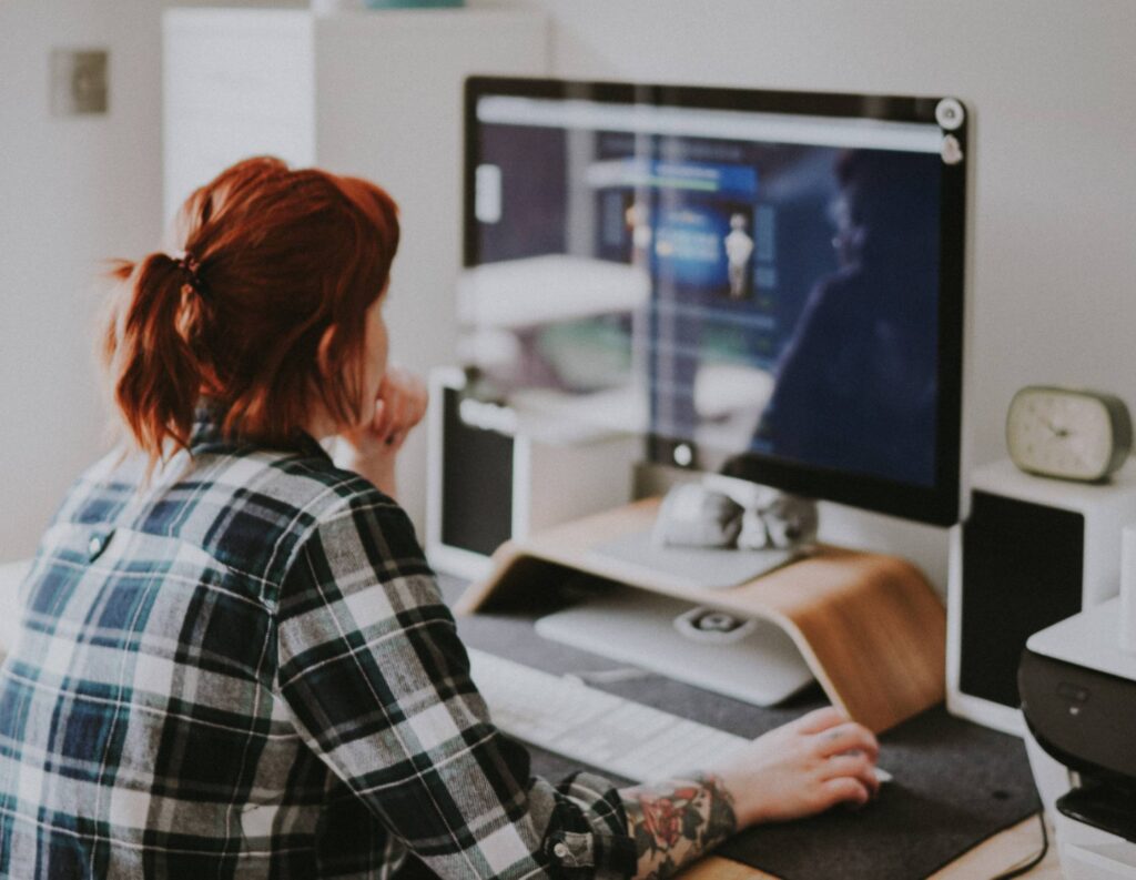 A woman with dark red hair sits facing a computer monitor where she's branding a website design