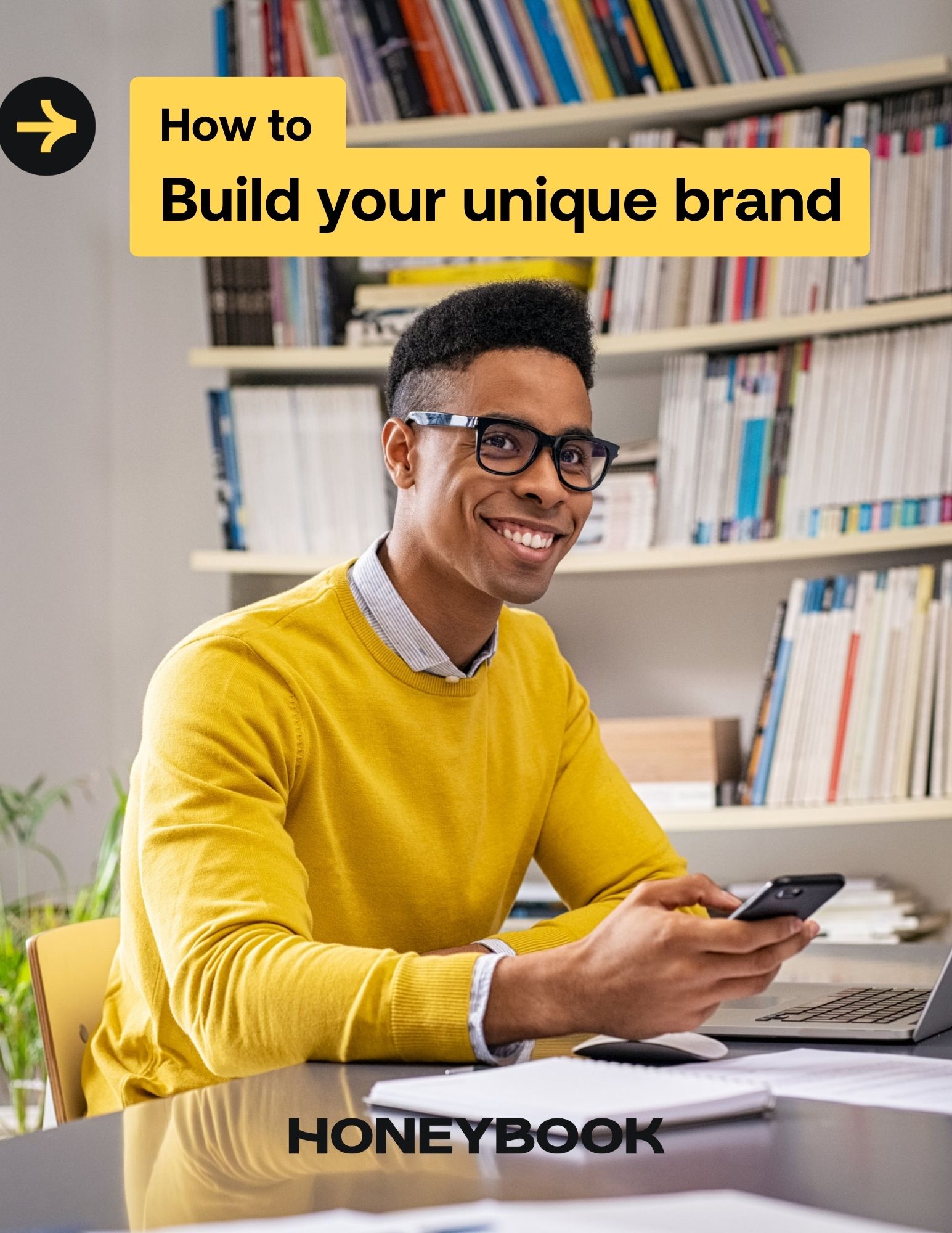 Man sits and smiles using phone in front of library on the cover of the build your unique brand guide.