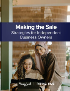 Two young woman lean over a computer studying sales strategies.