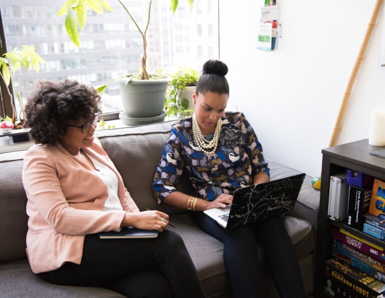 Two women sitting on a couch assess their current pricing on the computer.