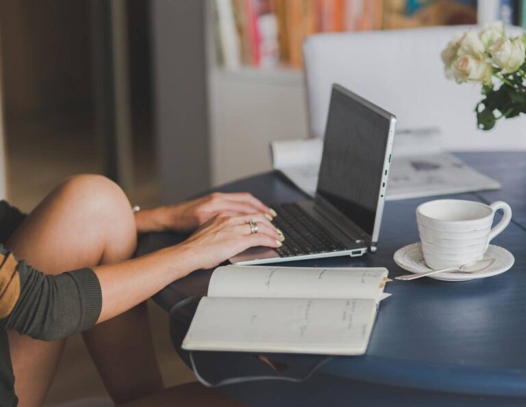 Person on laptop with notebook and coffee cup next to them