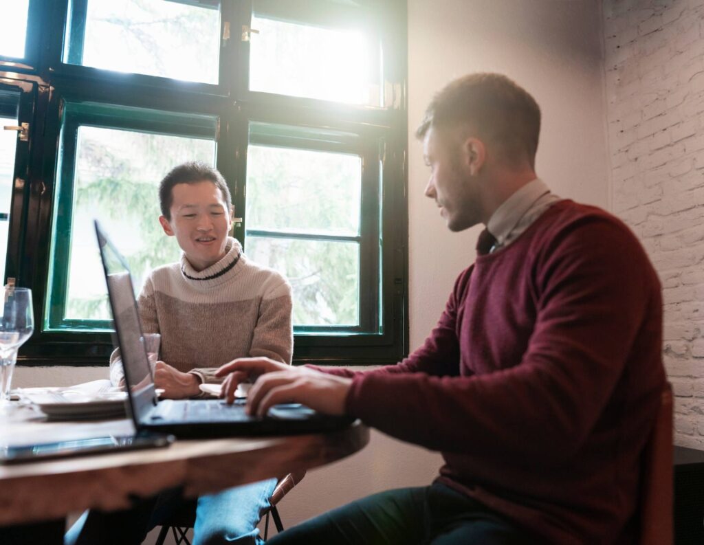 A man selling services to another man while at a table with a laptop