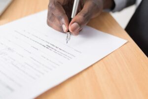 Close-up of a person signing a legal contract with a pen on a wooden desk