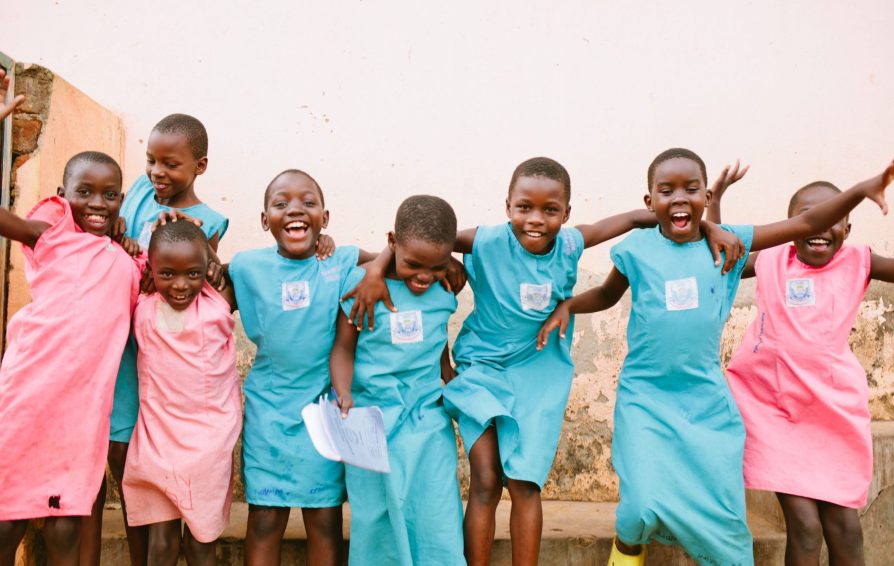 A group of children in colorful uniforms jump and smile together.