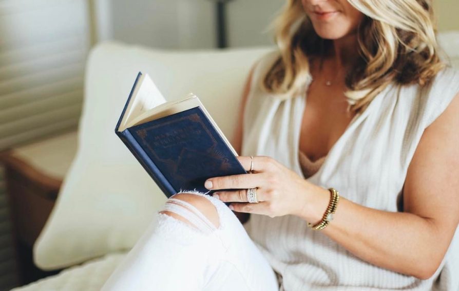 A woman sits on a couch, reading a book.