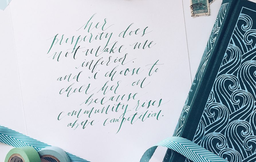 Calligraphy on a piece of paper taped to a surface, surrounded by washi tape, stamps, and a book
