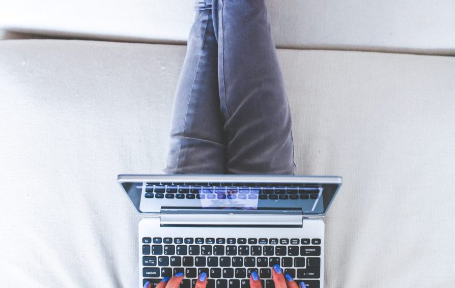 An aerial view of a woman lounging on a soft surface, working on a laptop