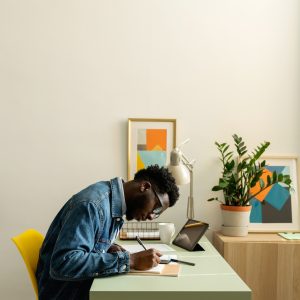 Side view of stylish black man in denim jacket working with documents at modern place with natural plants