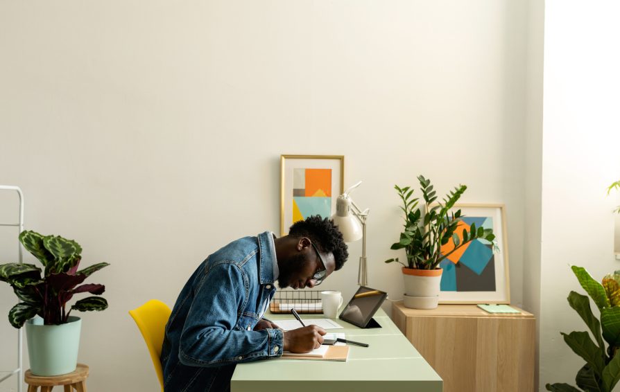 Side view of stylish black man in denim jacket working with documents at modern place with natural plants