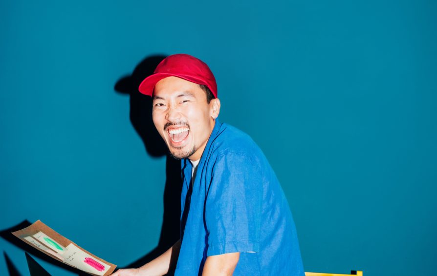 Portrait of handsome casually dressed asian man sitting in his office, holding his paperwork, working, looking at camera and smiling