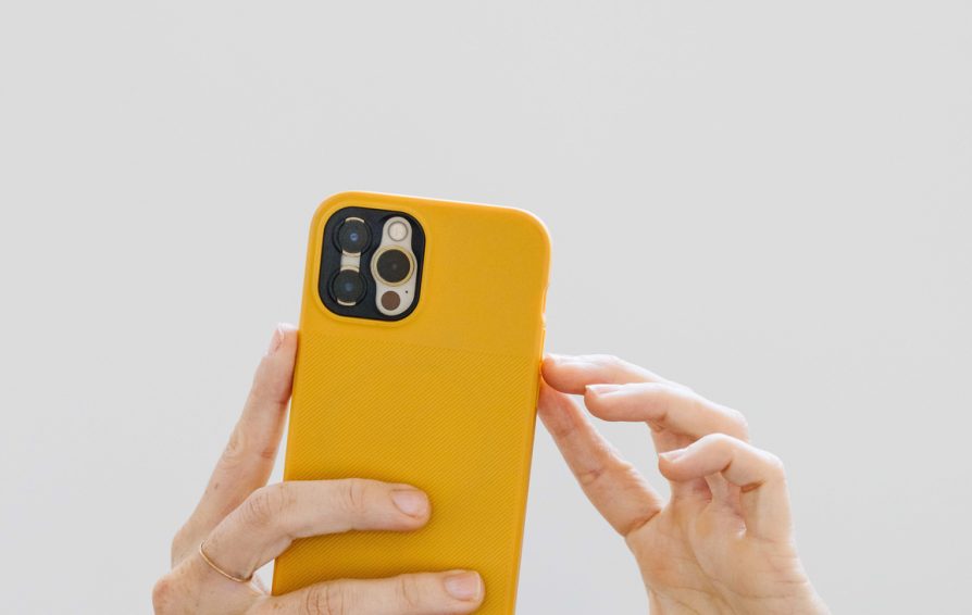 A woman's hand snapping a photo with her phone against a simple white background.