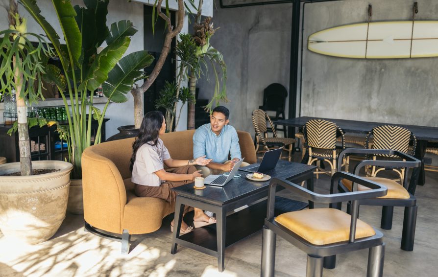 Colleagues sitting in a couch of a modern coffee shop, drinking coffee and working with laptop