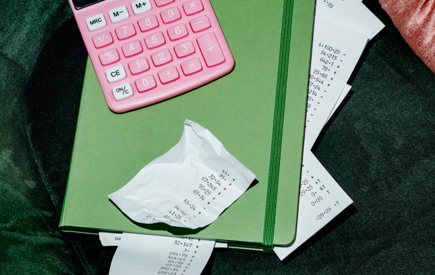 high angle view of a pink electronic calculator and some strips of paper with different calculations peeking out from a green notebook, placed on a green velvet chair