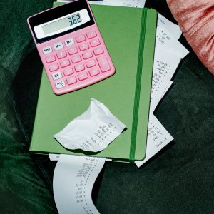 high angle view of a pink electronic calculator and some strips of paper with different calculations peeking out from a green notebook, placed on a green velvet chair