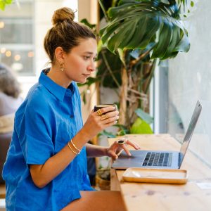 Young female entrepreneur, digital nomad, working remotely sitting in a cafe using laptop.