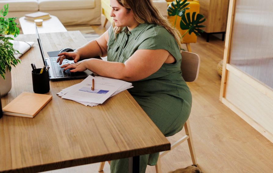 Female entrepreneur sitting at a table in her home office, typing on a laptop with her pug sleeping under the table
