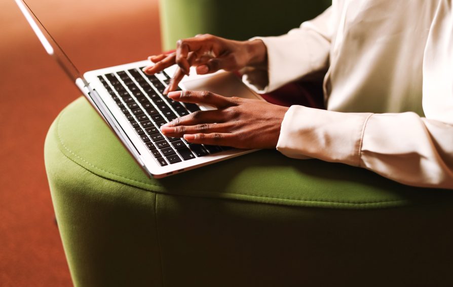 A professional woman works on her laptop, her hands poised over the keyboard. The sleek device and elegant attire reflect a productive and sophisticated setting.