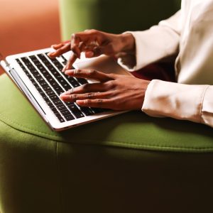 A professional woman works on her laptop, her hands poised over the keyboard. The sleek device and elegant attire reflect a productive and sophisticated setting.