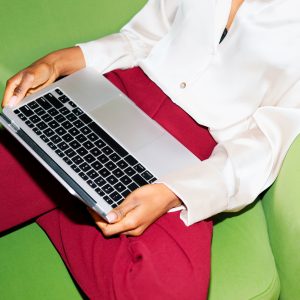 6646729 A woman working on laptop in elegant attire sits on a green chair. The modern workspace setting suggests productivity and remote work.