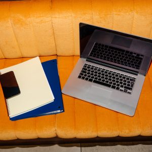Laptop with pen, smartphone, and notepads placed on cushioned orange in modern interior