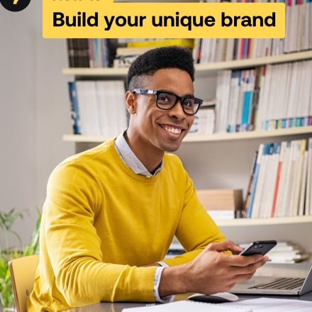 Man sits and smiles using phone in front of library on the cover of the build your unique brand guide.