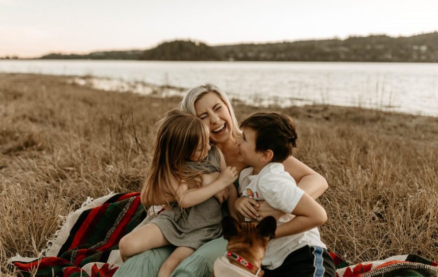 Young mom hugging and tickling her two kids in a field.