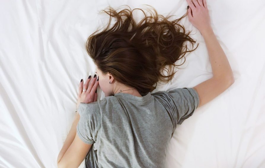 woman in a grey shirt laying on a white bedsheet