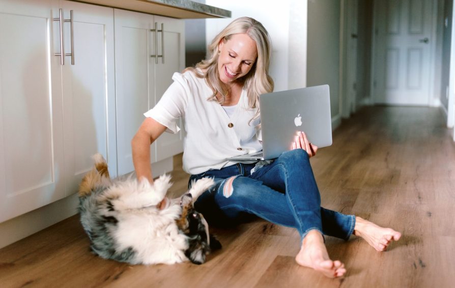 a woman sitting on the floor holding her laptop and petting a dog