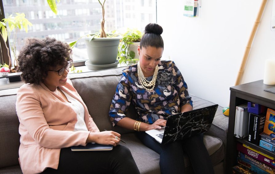 Two women sitting on a couch assess their current pricing on the computer.