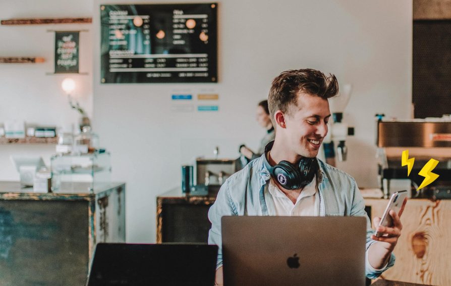 Man uses his phone and computer in a cafe.