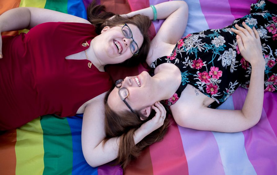 two women smiling and laying on a pride flag