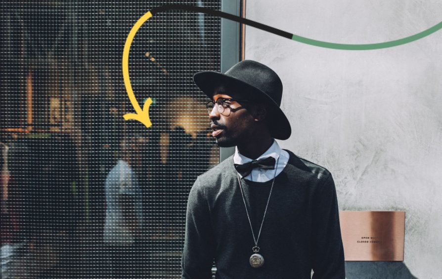 Stylish black man stands in front of department store looking to his right.