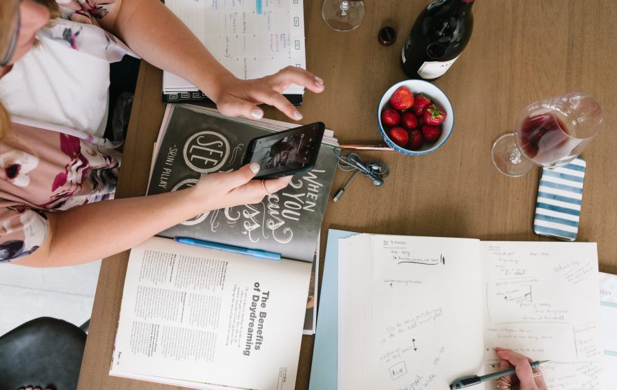 Aerial view of two people working at a table with wine, strawberries, and an assortment of papers.