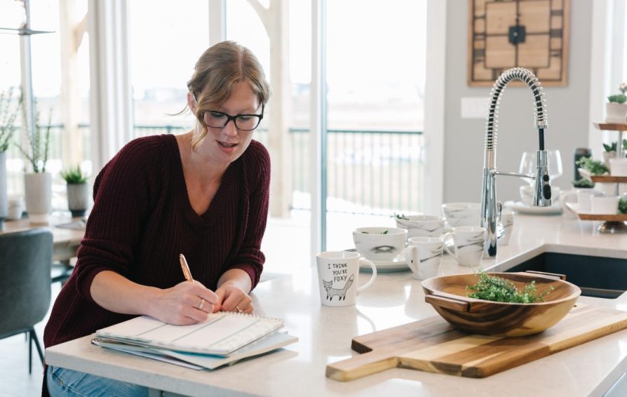 a woman sitting at her kitchen counter writing in a notebook