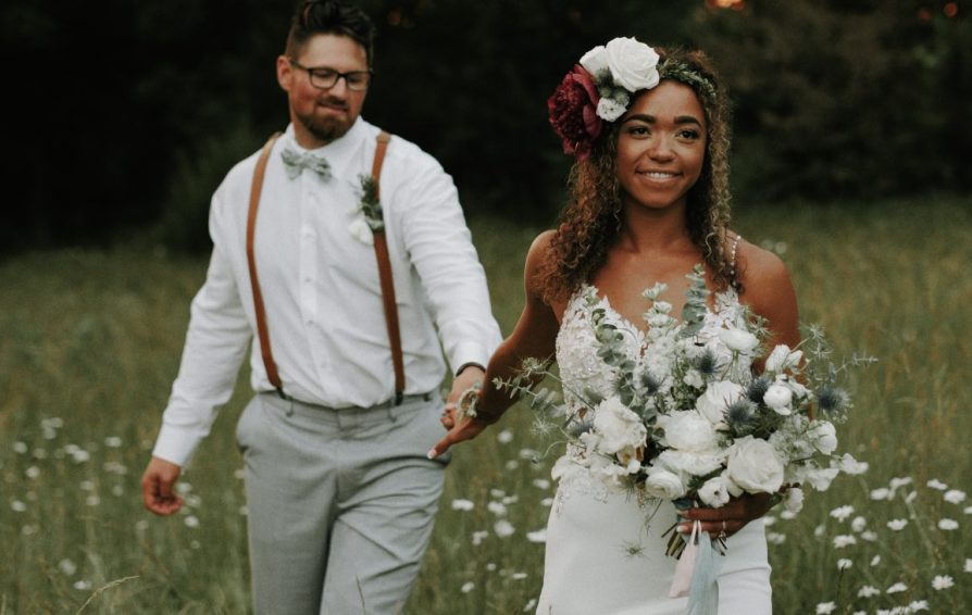 married couple in a field, holding hands and looking past the camera