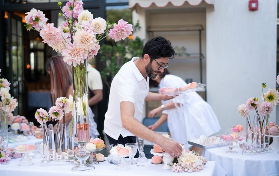 a man holding a tray of macaroons setting a table with flowers on it