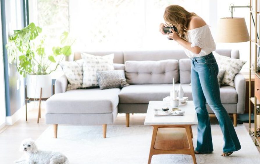woman in a living room pointing her camera down at a setting on a coffee table