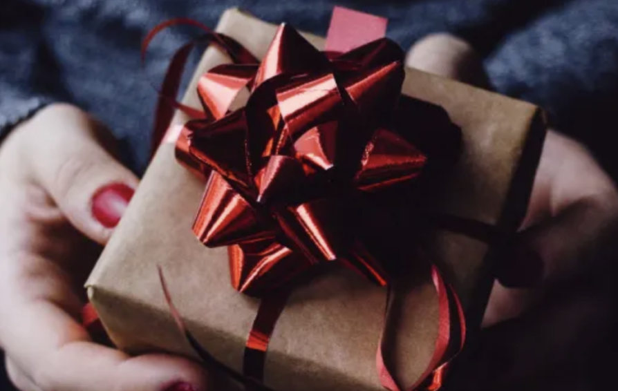 a woman's hands holding a branded gift for a client in a brown box with a red bow