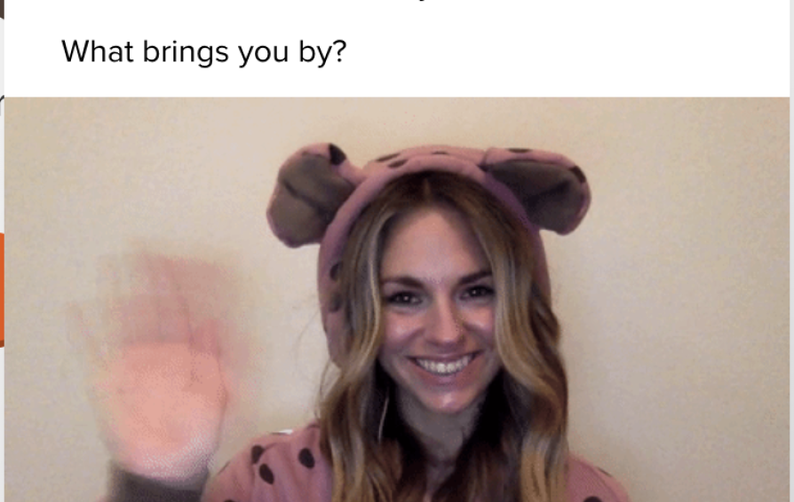 Inside an instant message window, a woman wears a polka-dotted jumper with a bear hoodie, waving at the camera