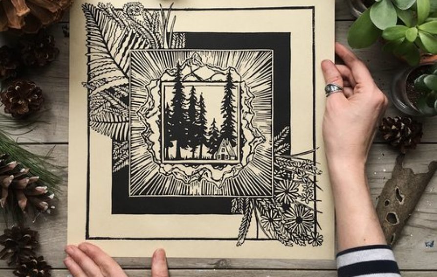 A pair of hands hold an ink drawing, surrounded by plants and acorns.