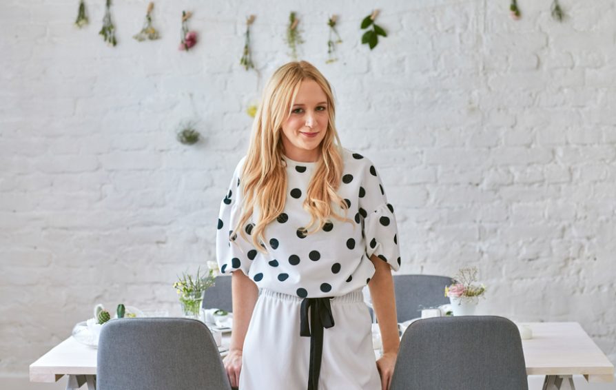 Pretty blonde elegant Caucasian woman standing by the dining table and looking at camera.