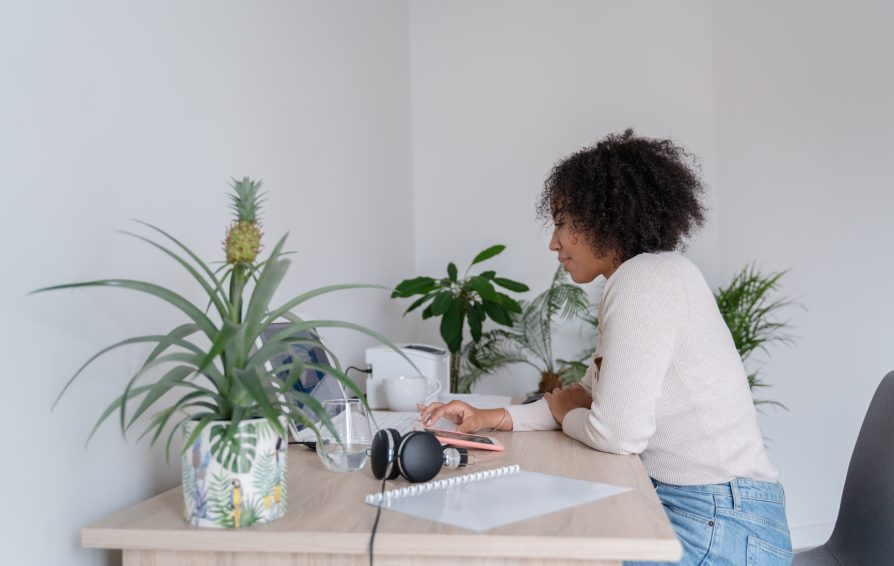 a woman sitting at a desk with plants tapping on her smartphone