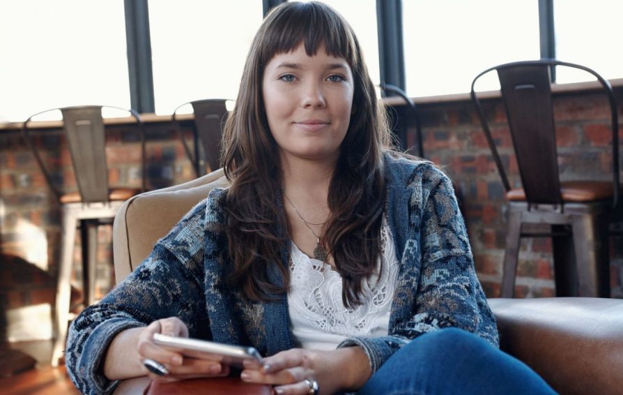 Woman with long brown hair smiles while holding phone.