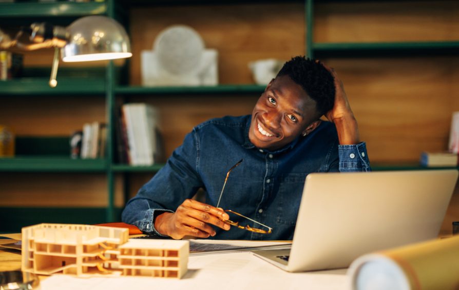 Young Architect smiles while at desk.