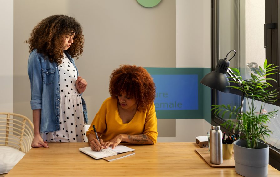 feminist multiethnic female co-workers working  together and taking notes on notebook in a modern and bright office
