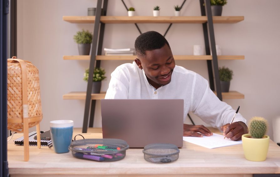 One Black delighted businessman in white shirt taking notes on paper sitting in modern office at his desk.
