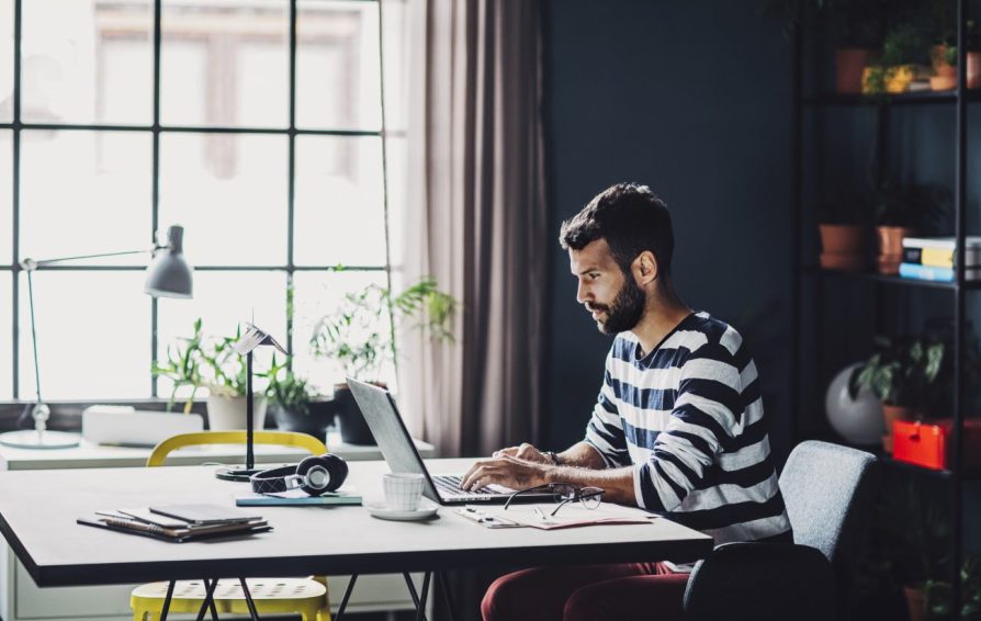 Man in a striped shirt working on a laptop.