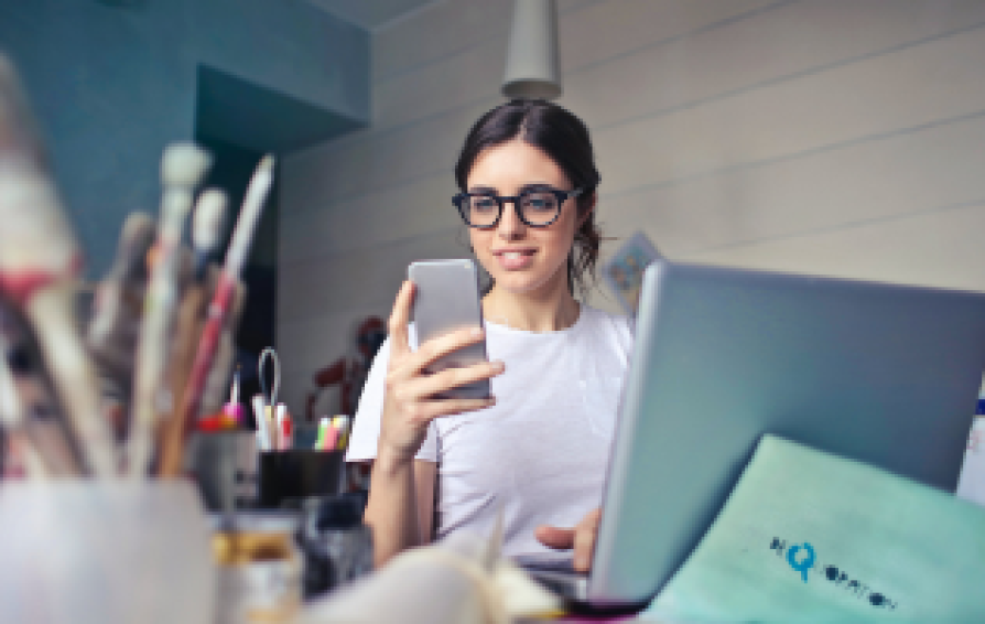 Small business owner on laptop and looking at smartphone to track time