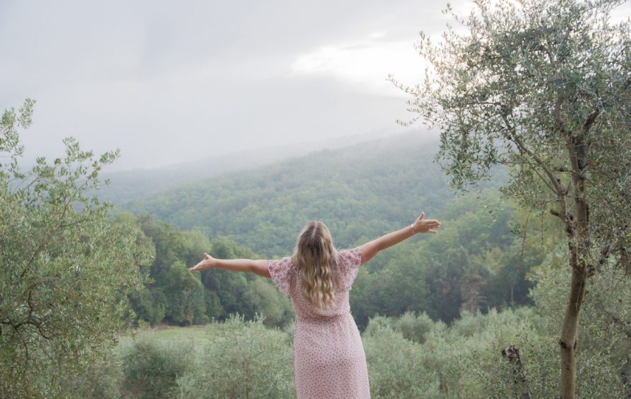 woman with her arms outstretched in front of a wooded hill